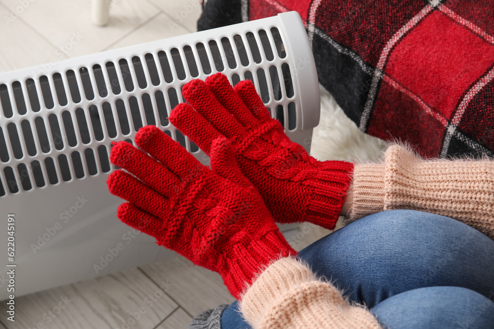 Woman warming hands in gloves near radiator at home, closeup