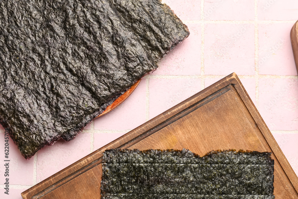 Wooden board of nori on pink tile background, closeup