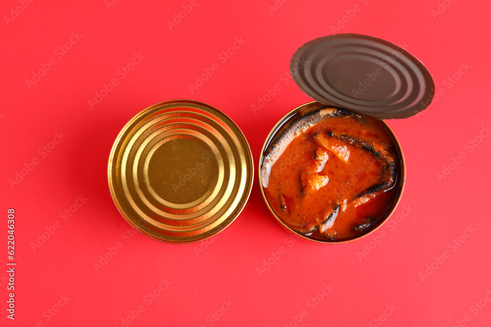 Tin cans with fish in tomato sauce on red background