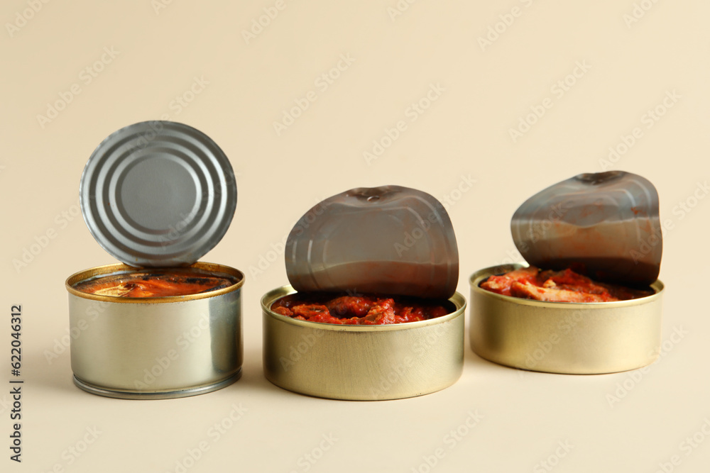 Opened tin cans with fish in tomato sauce on beige background