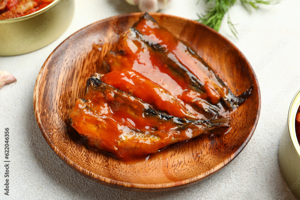 Wooden plate with canned fish in tomato sauce on white table, closeup