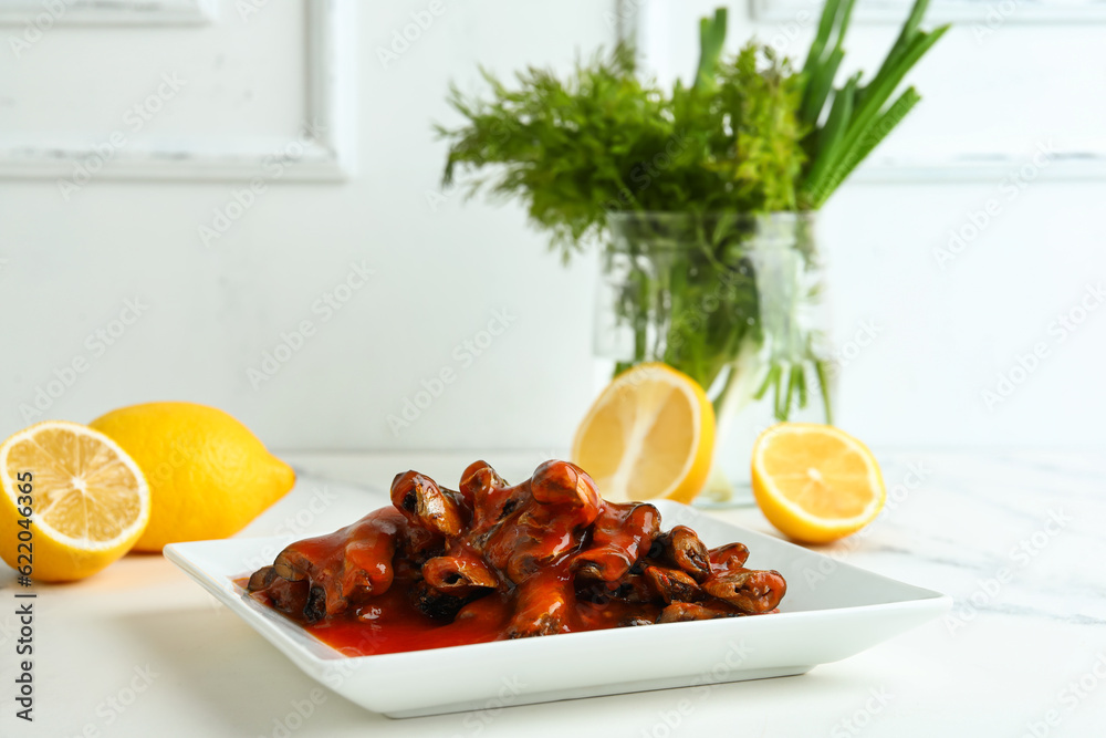 Plate with canned fish in tomato sauce and lemons on white table