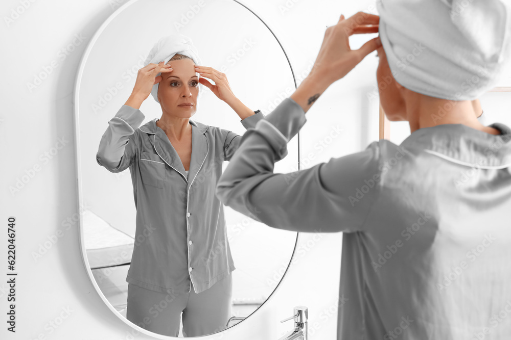 Mature woman doing face building exercise near mirror in bathroom