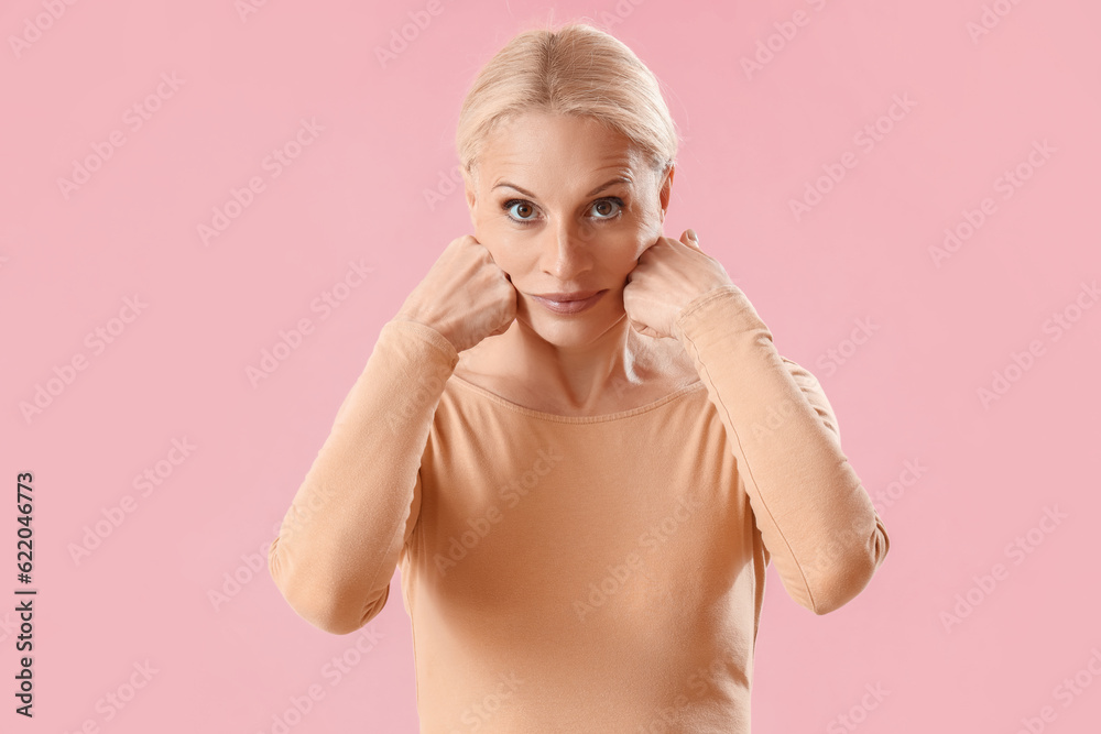 Mature woman doing face building exercise on pink background