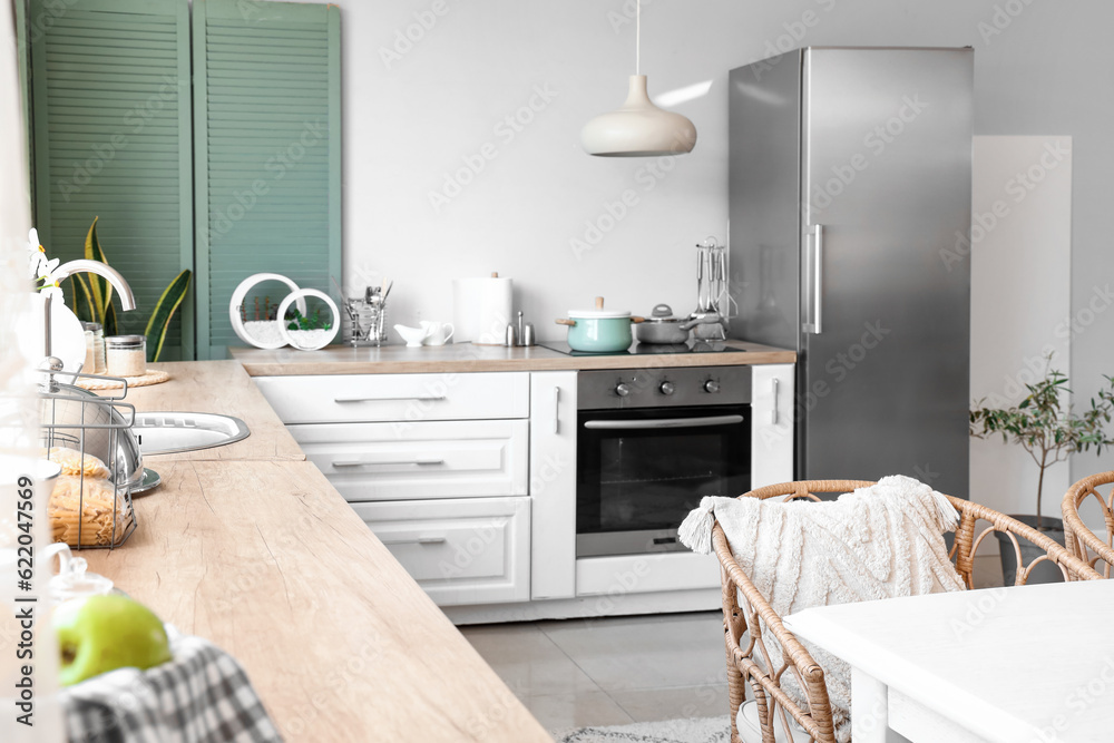 Interior of light kitchen with stylish fridge, counters, table and chair