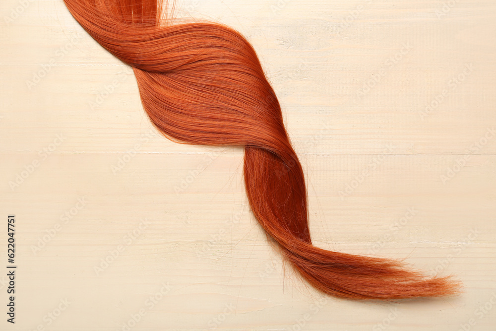 Ginger hair strand on light wooden background, closeup