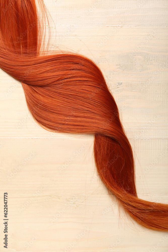 Ginger hair strand on light wooden background, closeup