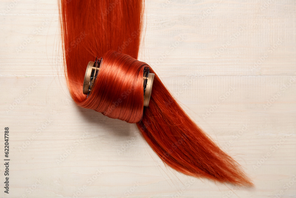 Ginger hair strand with curler on light wooden background, closeup