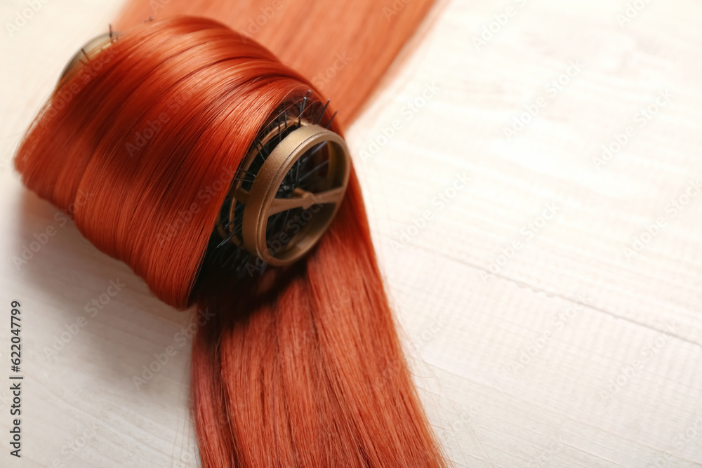 Ginger hair strand with curler on light wooden background, closeup