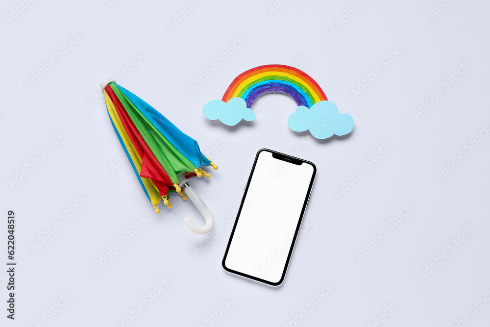 Mobile phone with umbrella and paper rainbow on white background. Weather forecast concept