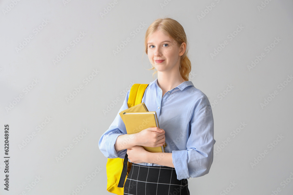 Female student with backpack and books on grey background