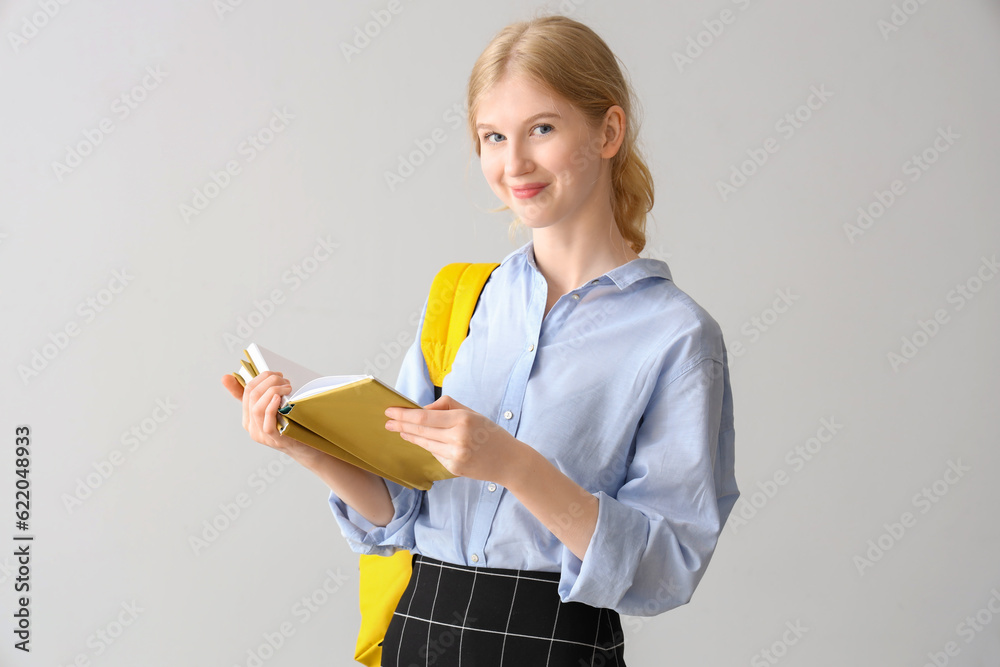 Female student with backpack reading book on grey background