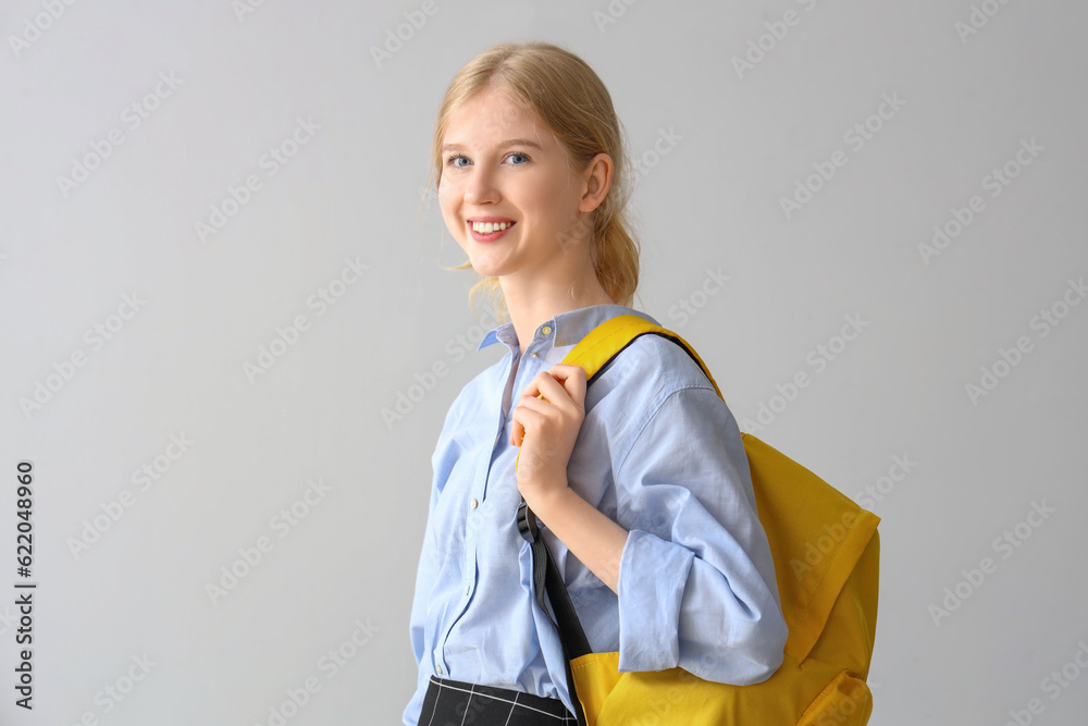 Female student with backpack on grey background