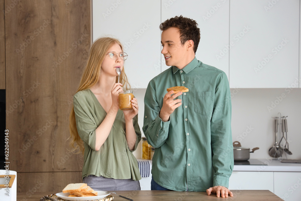 Young woman eating nut butter and handsome man with bread toast in kitchen