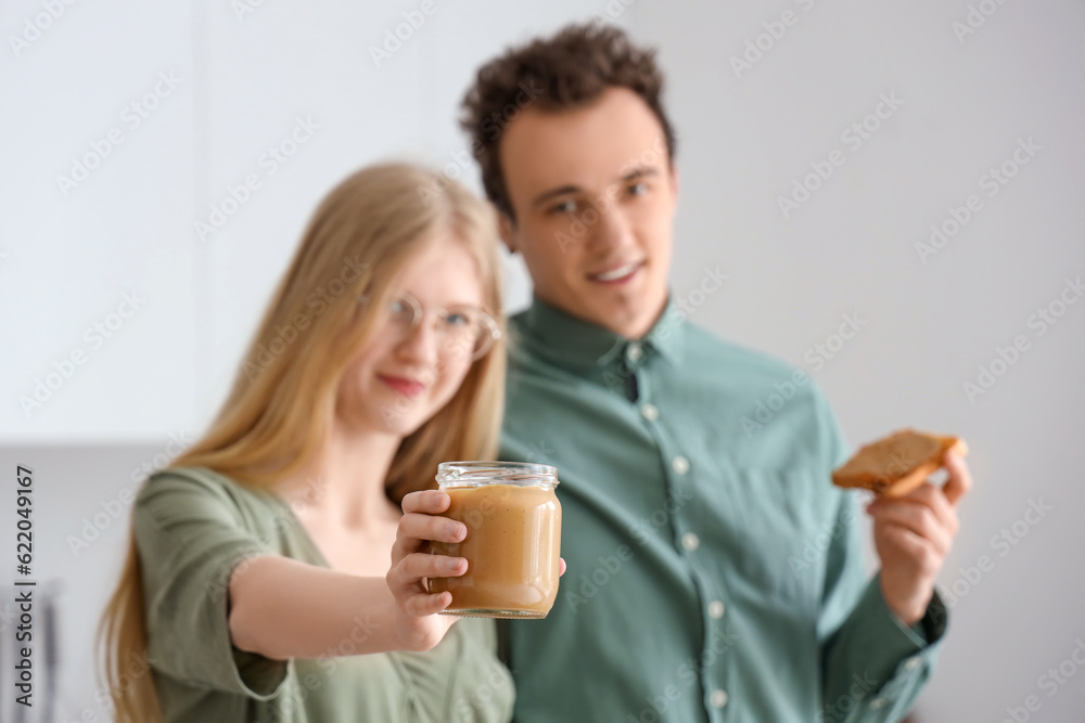 Young woman holding jar of nut butter and handsome man with toast in kitchen