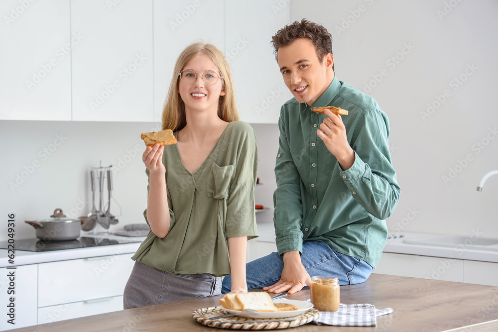 Happy young couple with tasty toasts of nut butter in kitchen