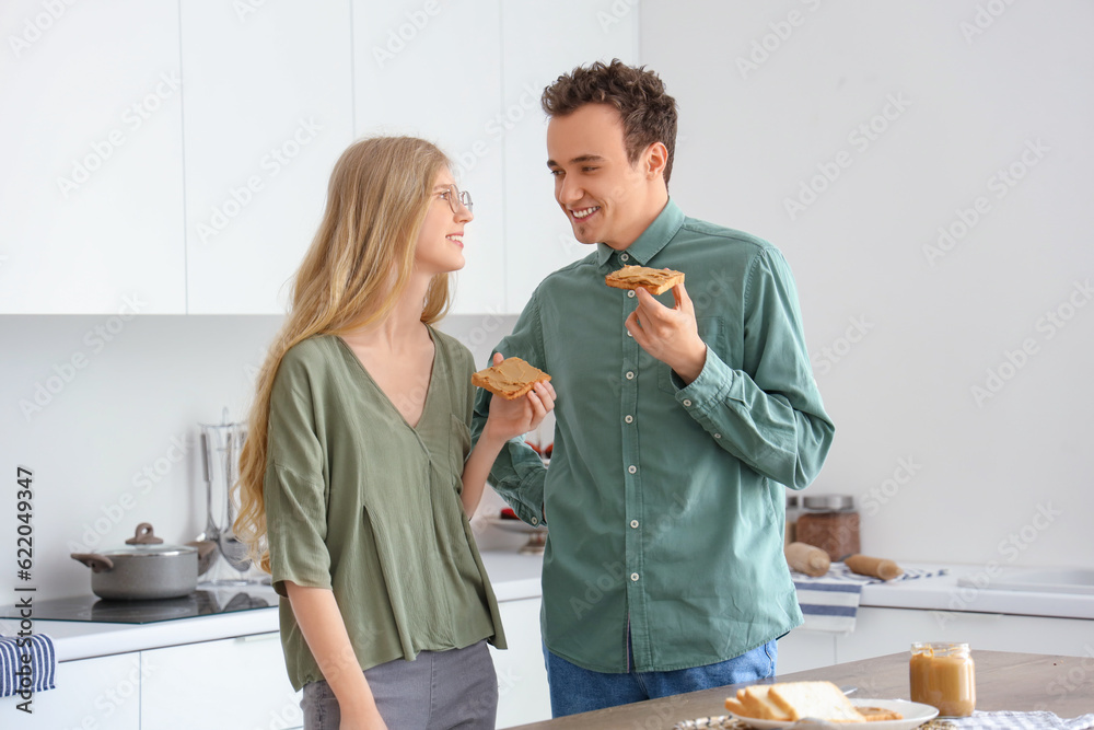 Happy young couple with tasty toasts of nut butter in kitchen