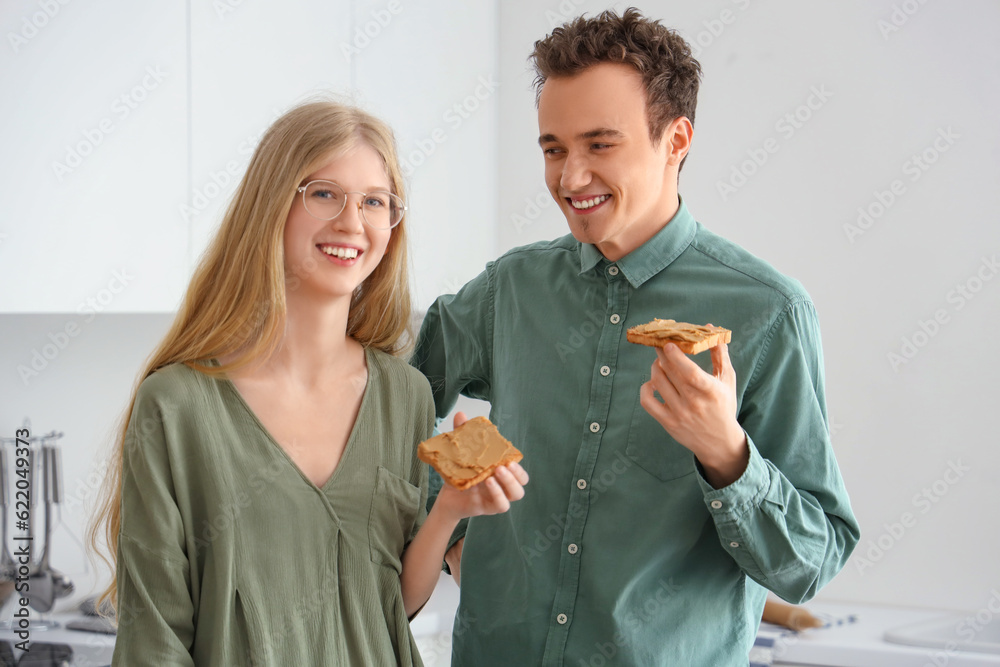 Happy young couple with tasty toasts of nut butter in kitchen