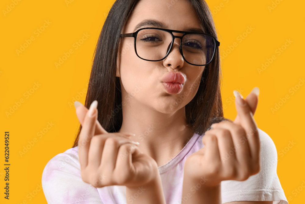 Pretty young woman wearing glasses and making hearts with her fingers on yellow background