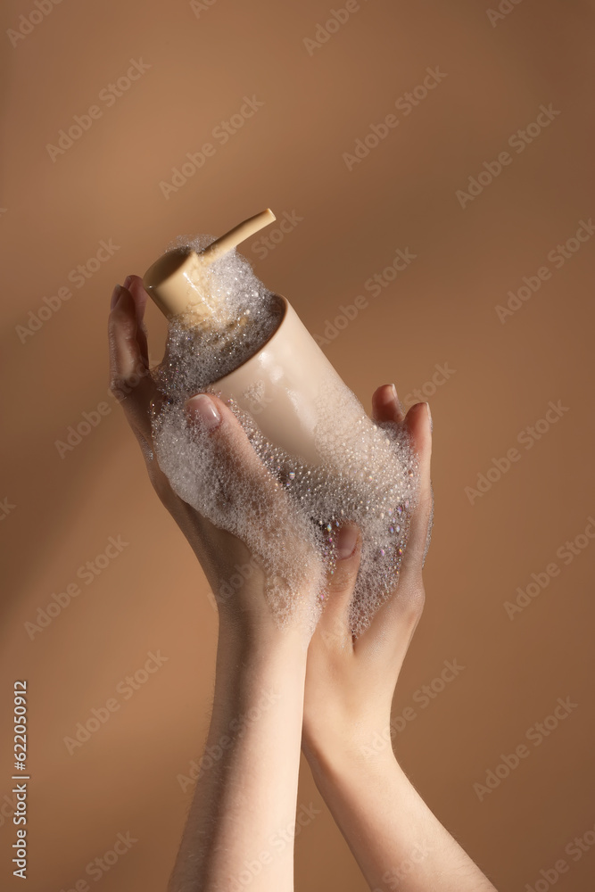 Hands with liquid soap on brown background