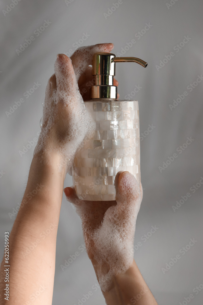 Hands with liquid soap on grey background