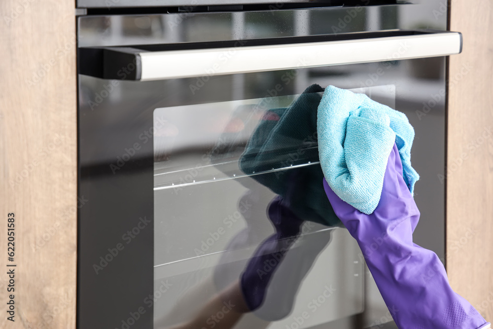 Woman cleaning electric oven with sponge in kitchen, closeup