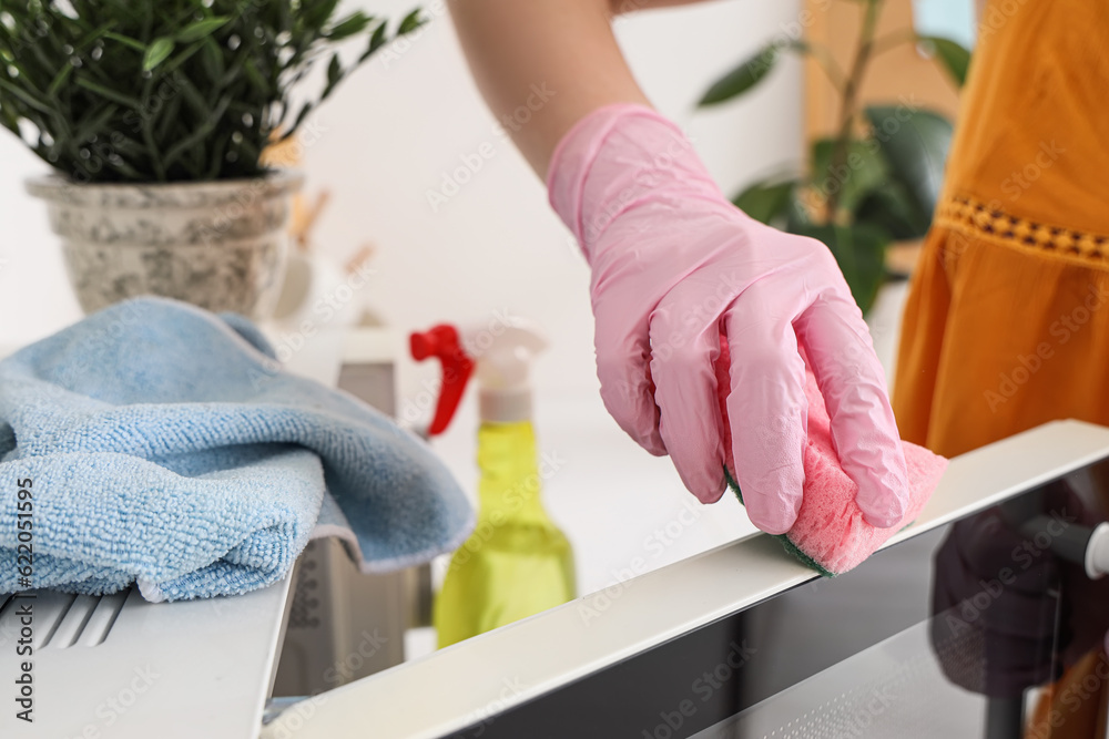 Woman cleaning microwave oven with sponge in kitchen, closeup