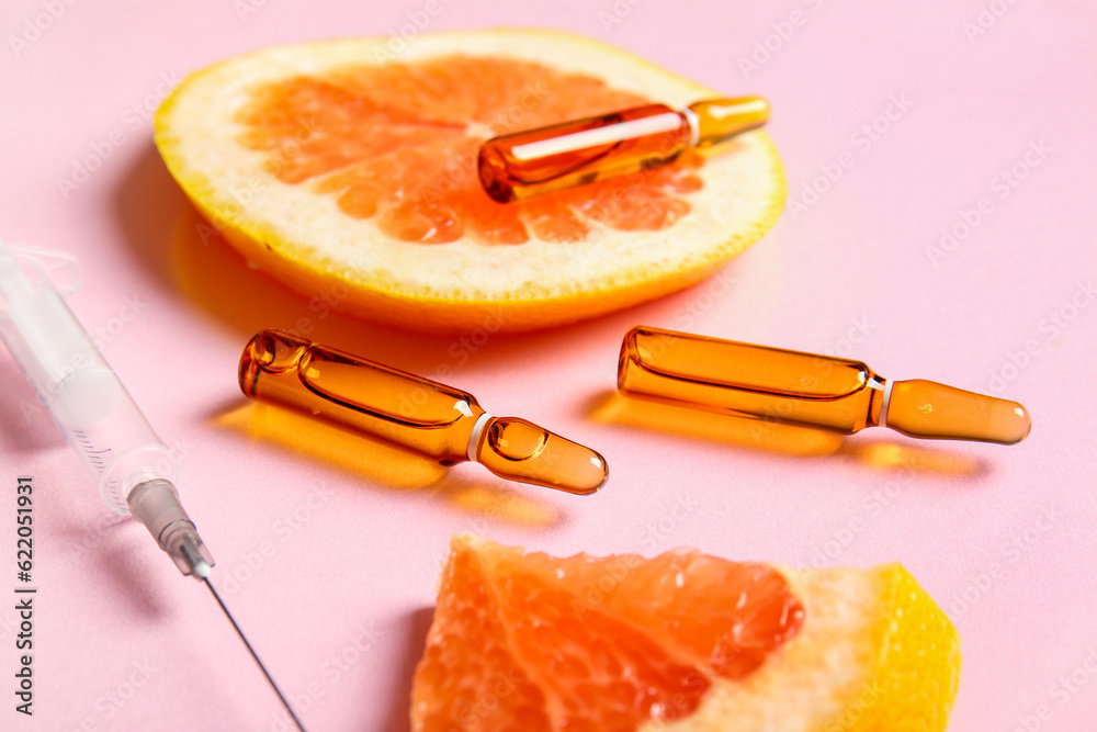 Ampoules with vitamin C and grapefruit slices on pink background