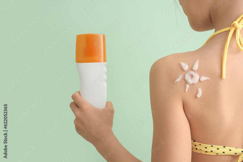 Little girl with bottle of sunscreen cream on pale green background