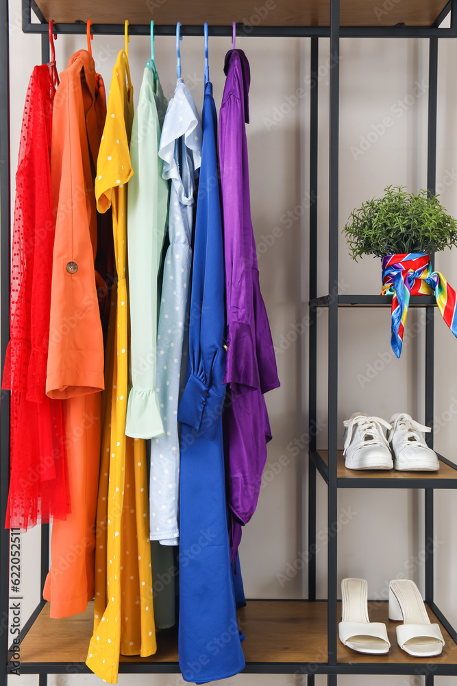 Shelving unit with colorful clothes, shoes and houseplant near white wall, closeup