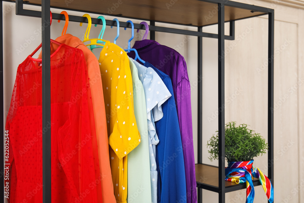 Shelving unit with colorful clothes and houseplant near white wall