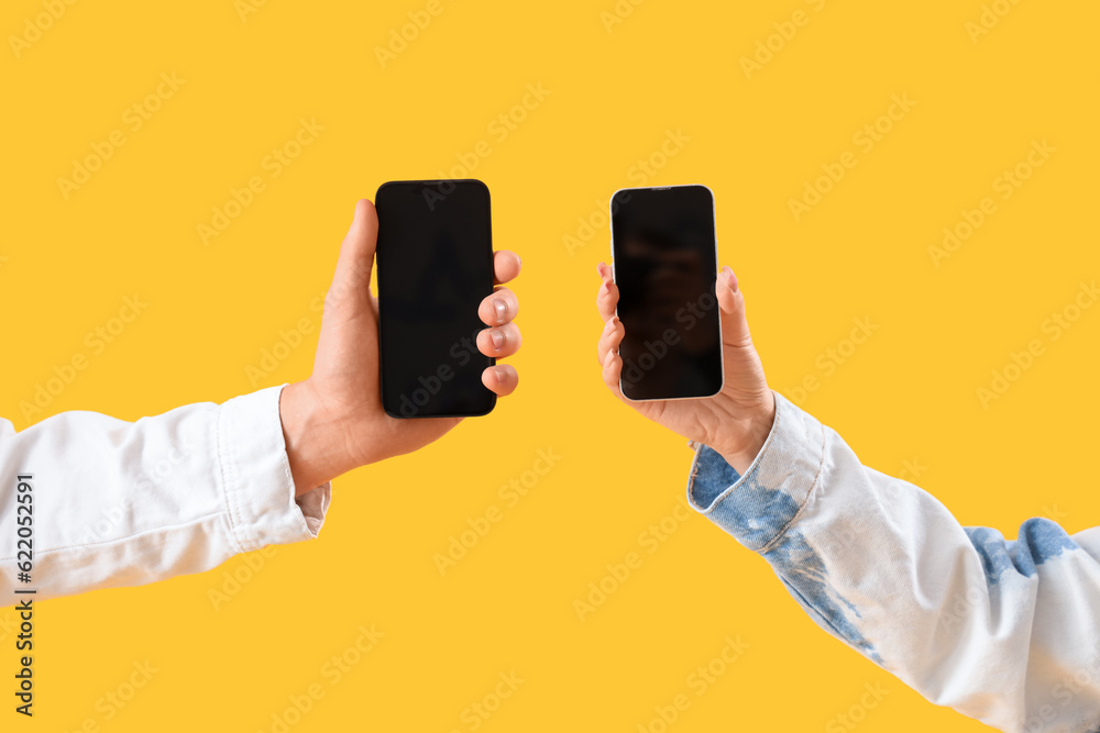 Young couple with mobile phones on yellow background