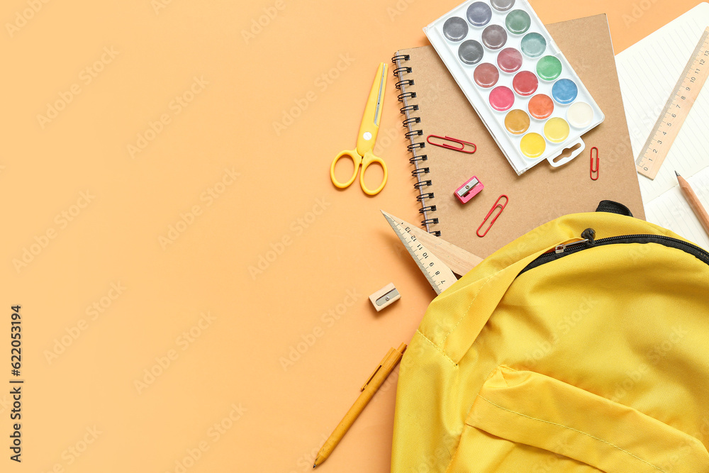 School backpack with paints and stationery on orange background