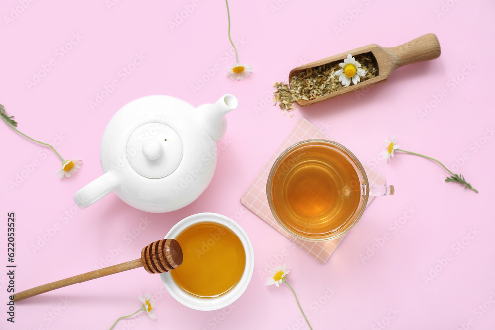 Teapot and cup of hot chamomile tea with honey on pink background