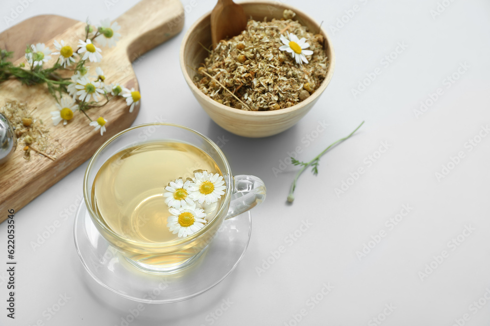 Cup of hot tea and bowl with dried chamomile on white background