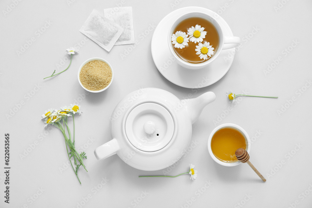 Teapot and cup of hot chamomile tea with honey on white background