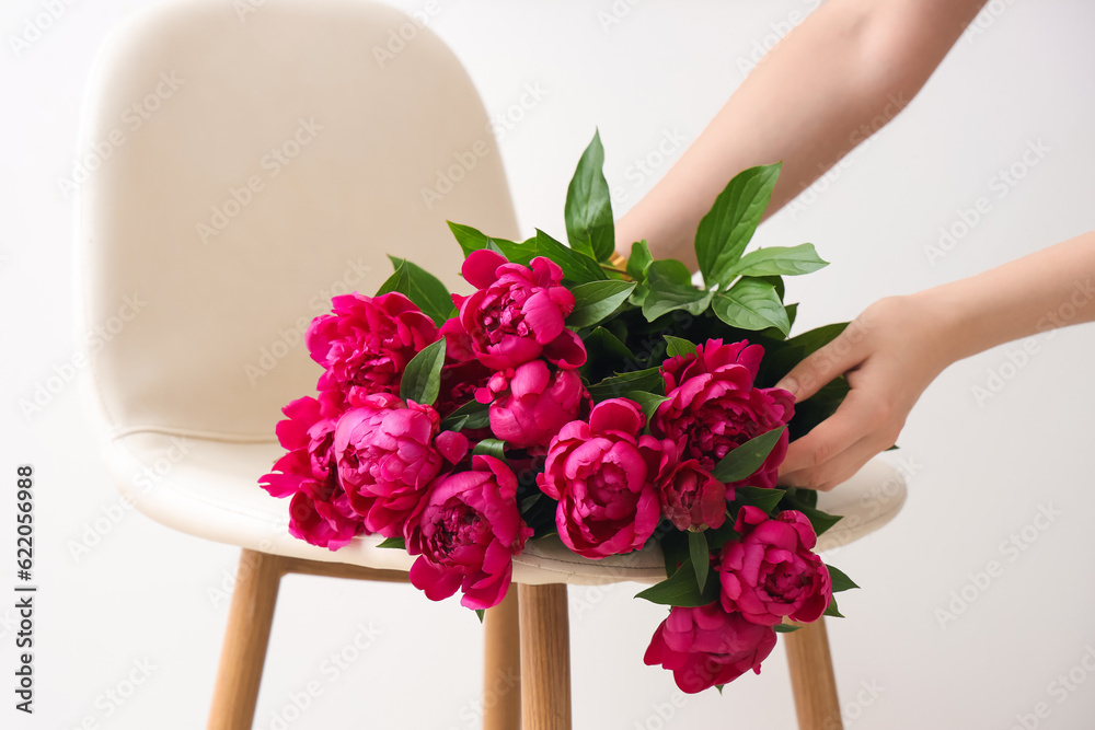 Female hands with red peonies and chair near white wall in living room