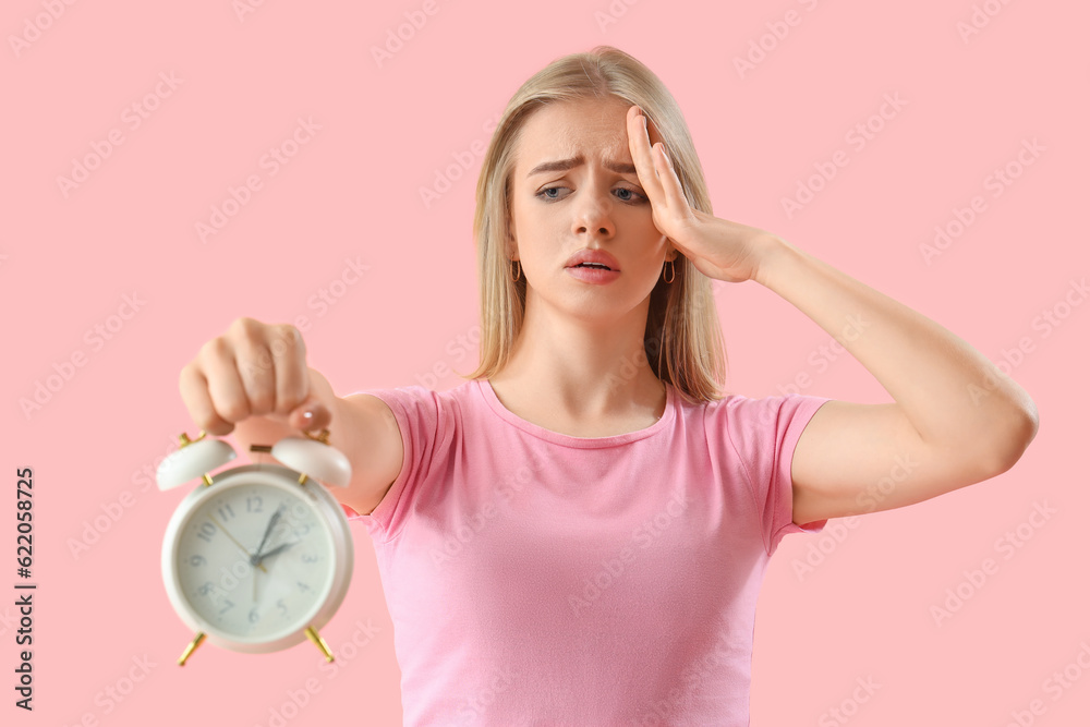 Stressed young woman with alarm clock on pink background. Deadline concept