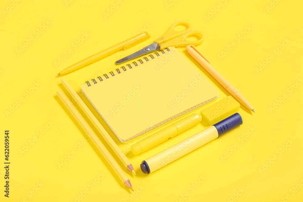 Notebook with different stationery on yellow background