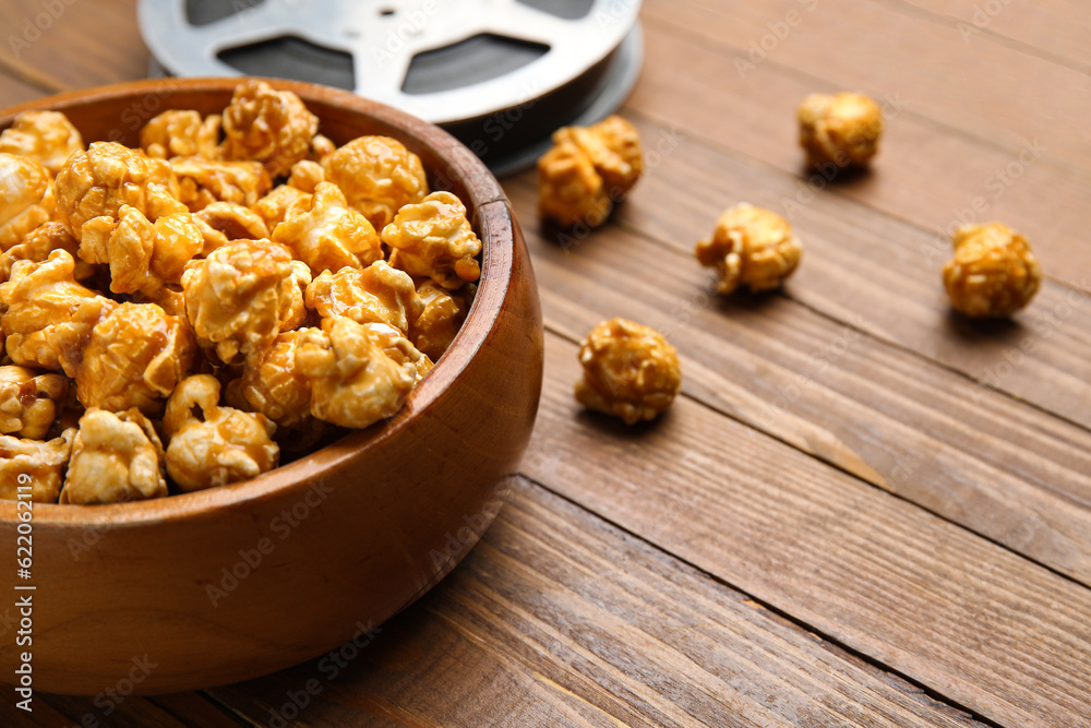 Bowl with tasty popcorn and film reel on wooden background