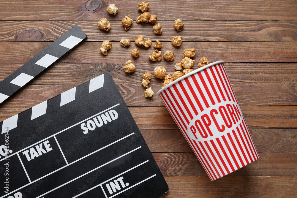 Bucket with tasty popcorn and clapperboard on wooden background