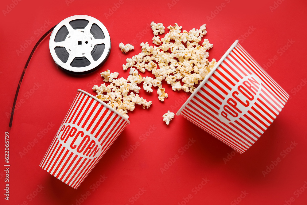 Buckets with tasty popcorn and film reel on red background