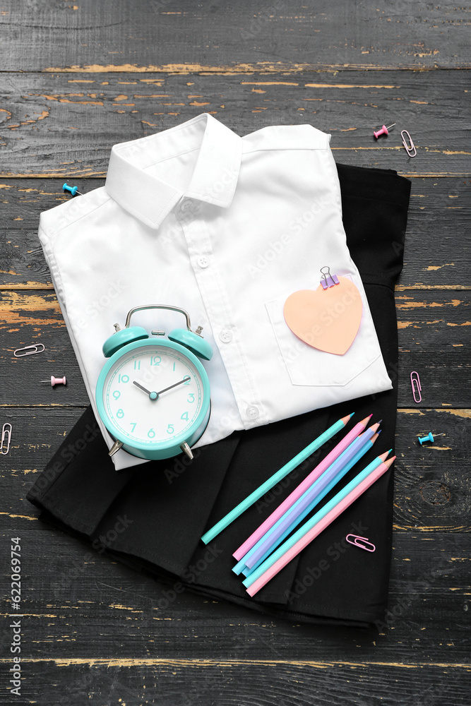 Different stationery with stylish school uniform and alarm clock on brown wooden background