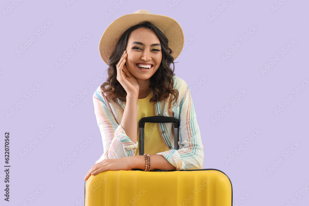 Young woman in summer hat with suitcase on lilac background