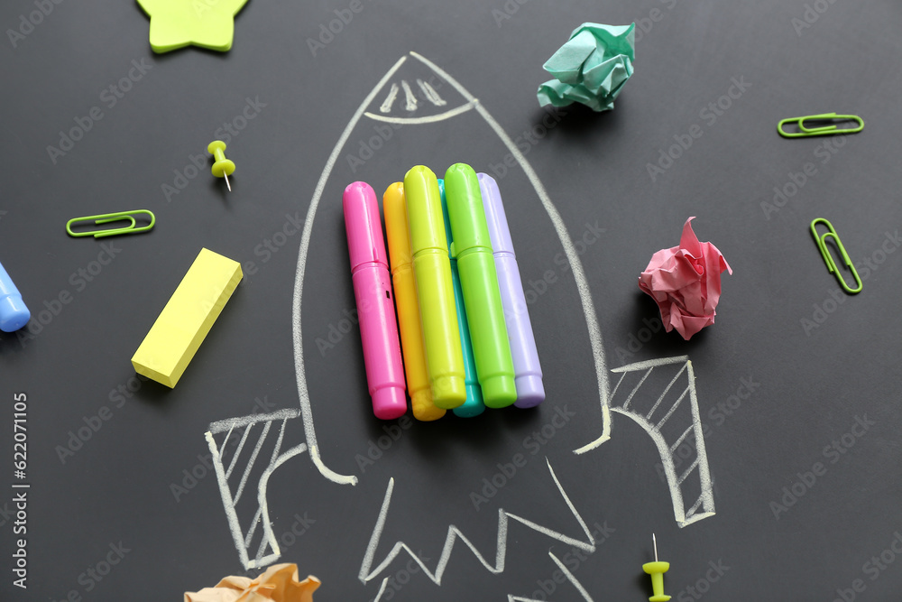 Drawn rocket with different stationery on black chalkboard