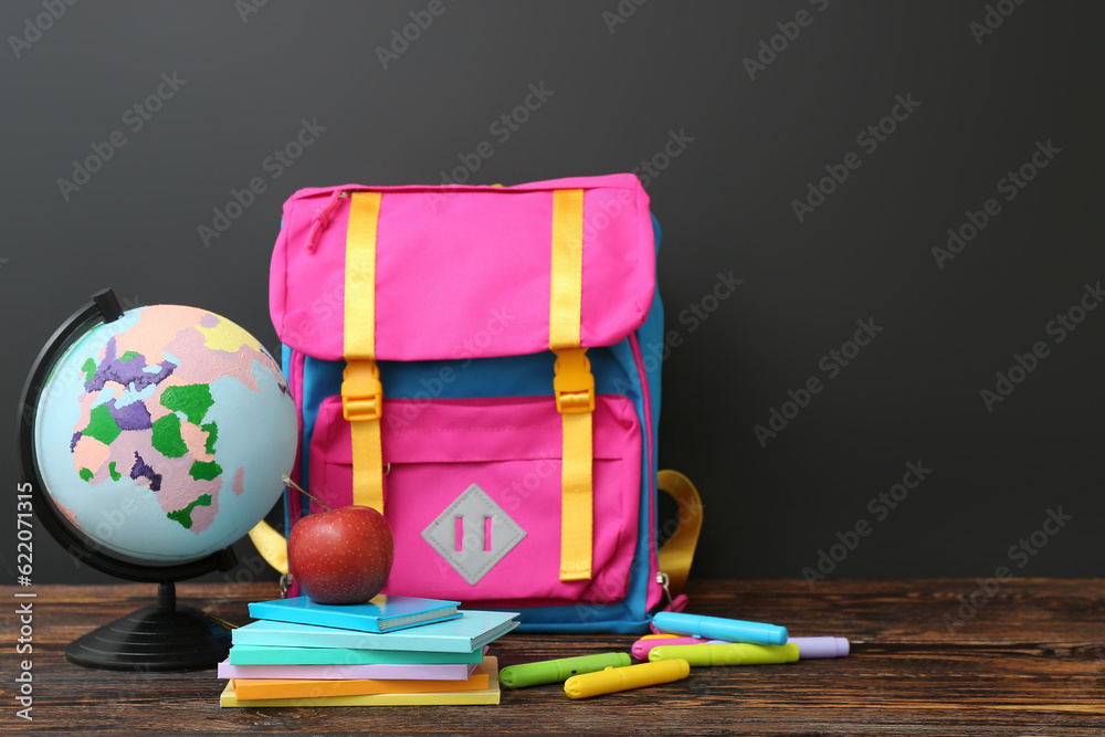 Backpack with different stationery and globe on wooden table against black chalkboard