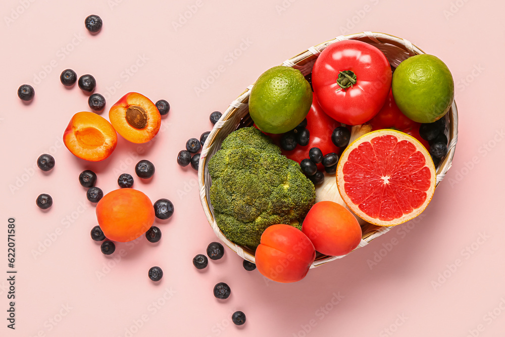 Wicker bowl with different fresh fruits and vegetables on pink background