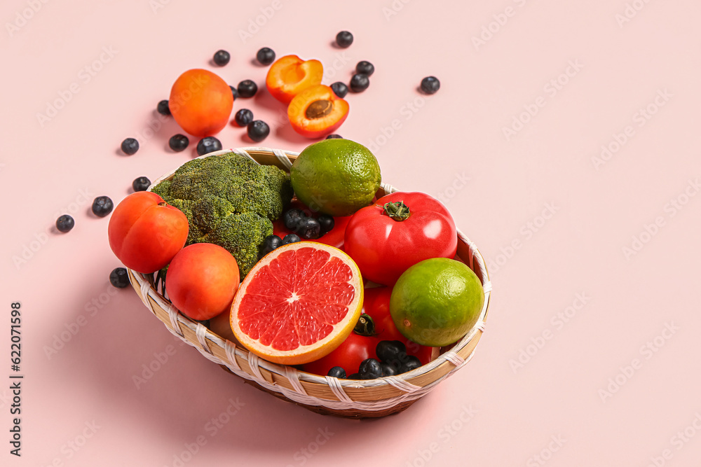 Wicker bowl with different fresh fruits and vegetables on pink background