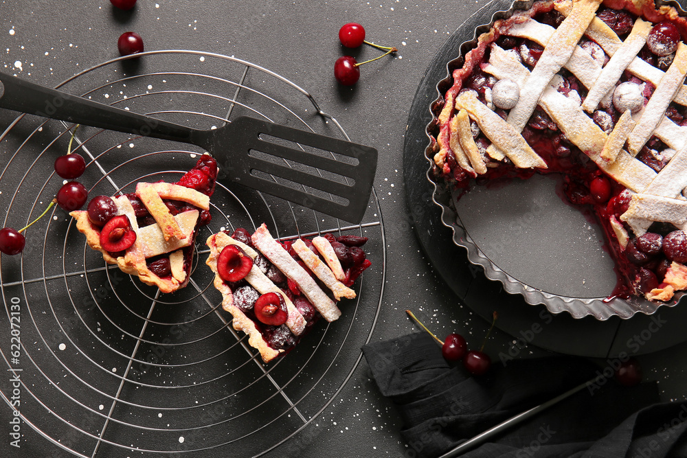 Baking dish with tasty cherry pie and stand of pieces on black background