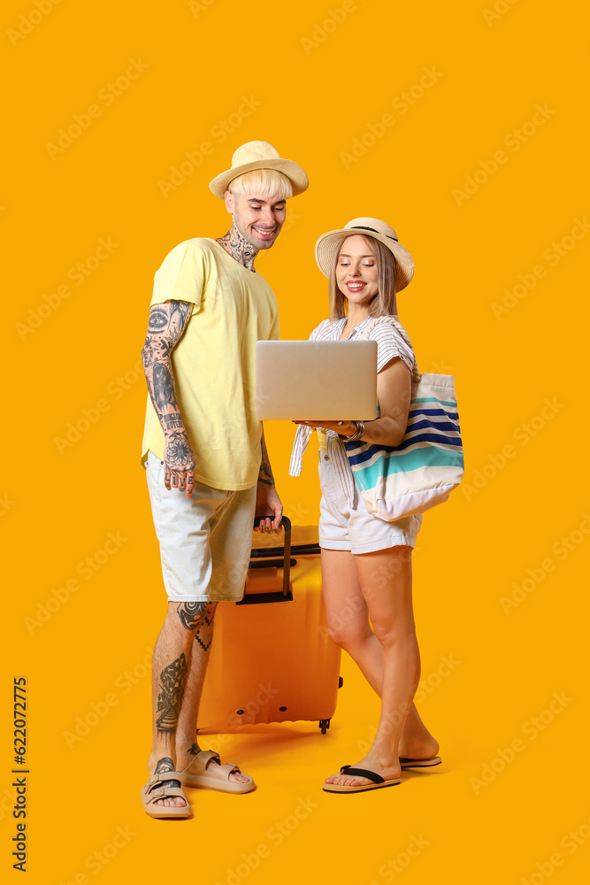 Young couple with laptop and suitcase on yellow background